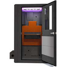 Load image into Gallery viewer, Front view of WhisperRoom's Voice Over Basic Package - a 4' x 4' single-wall vocal booth, thoughtfully equipped with acoustic treatment, a functional desk, studio lighting, and a variety of premium features. The right-hinged door is open, revealing the interior adorned with vibrant orange StudioFoam, creating an inviting recording space.