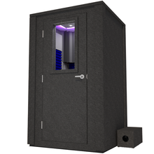 Load image into Gallery viewer, Angled view of the WhisperRoom's Voice Over Deluxe Package - a 4' x 4' double-wall vocal booth, meticulously designed with acoustic treatment, a functional desk, studio lighting, and a comprehensive range of premium features. The left-hinged door is closed, and the interior is accentuated with vibrant blue StudioFoam, creating an ideal recording environment.
