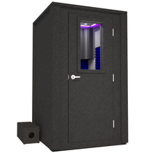 Load image into Gallery viewer, Angled view of the WhisperRoom's Voice Over Deluxe Package - a 4' x 4' double-wall vocal booth, meticulously designed with acoustic treatment, a functional desk, studio lighting, and a comprehensive range of premium features. The right-hinged door is closed, and the interior is accentuated with vibrant blue StudioFoam, creating an ideal recording environment.