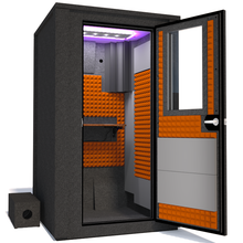 Load image into Gallery viewer, Angled view of the WhisperRoom's Voice Over Deluxe Package - a 4' x 4' double-wall vocal booth, meticulously designed with acoustic treatment, a functional desk, studio lighting, and a comprehensive range of premium features. The right-hinged door is open, revealing the interior enhanced by vibrant orange StudioFoam, creating an ideal recording atmosphere.